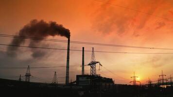 Electrical pylons near harmful factory at red sunset. Dark smoke released into the air from industrial pipe. Transmission lines. Pollution the environment. Camera moving down. video