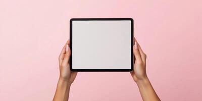 Female hands holding tablet with natural nails on soft pink background for technology and design concepts photo