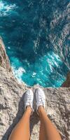 Adventure at coastal cliff. Female feet in white sneakers overlooking stunning ocean view photo