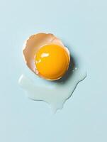 Cracked egg with yolk on light blue ceramic surface for culinary design photo