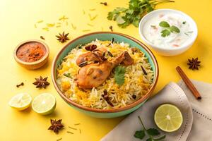 Delicious and aromatic chicken biryani with raita and chutney served in a vibrant yellow background a delightful presentation. photo