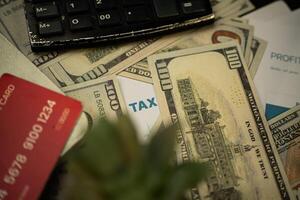 an image that focuses on a paper that says TAX surrounded by several dollar bills. Business and finance concepts photo