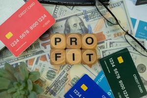 A wooden blocks with the word PROFIT written on it, surrounded by several credit cards, sunglasses and a black calculator, and underneath are several dollar bills. Concept of business and finance. photo