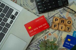 a red credit card placed on a laptop, some dollar bills, a black calculator and a wooden block that says PROFITABLE. finance and business backgrounds. photo