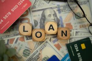 A wooden block with the word LOAN written on it, surrounded by several credit cards, sunglasses and a black calculator, and underneath are several dollar bills. Concept of business and finance. photo