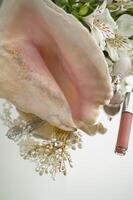 Pink lip gloss, highlighter in a beautiful jar, white lilies, hair ornaments with pearls, large seashell on a mirror background. Flat lay with space for text. photo