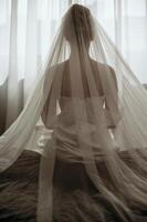 Close-up of a bride in a luxurious veil from the back. The bride in a white dress is sitting on a bed, she is wearing a large veil. Silhouette of a bride, view from the back photo