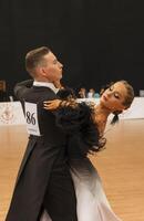 couple dancing standard European program on the dance floor. Young man in tailcoat, girl in black and white long dress and white shoes. Couple dancing Viennese waltz. tango photo