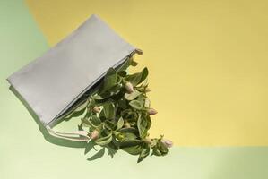 On a yellow and light green background, a women's white cosmetic bag with spring apple tree branches. The concept of cosmetics, spring, freshness. photo