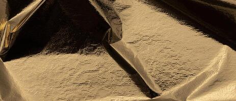 Golden foil with reflective, shiny folds creates a sleek, opulent design. Gilded, metallic texture photo