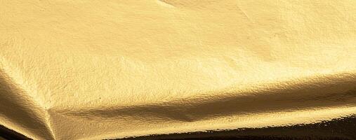 Gold metallic foil texture with a folded, smooth surface. Shiny, reflective material in warm yellow photo