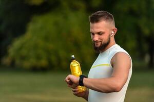 A happy runner man looking at a monitor watch checking heart rate while running or jogging in the park, active healthy lifestyle. photo