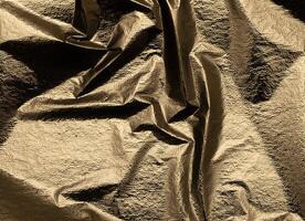 Gold foil fabric background with a sleek, crumpled texture. Shiny, soft surface with elegant folds, photo