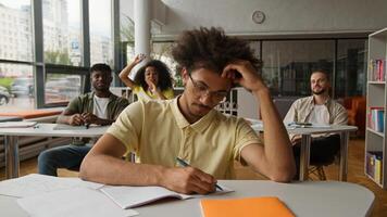 African American man student guy writing task in class lesson in classroom friends classmates bullying mocking bully throwing papers balls mockery laughing four students lecture in university college photo