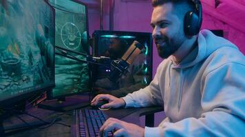 Addicted Caucasian guy male gamer streamer man play online battle enjoying smiling wearing headphones gaming at computer streaming in neon dark room at home match digital playing looking internet game photo