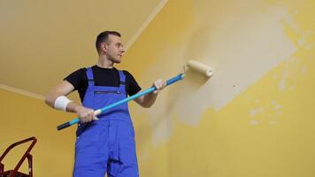 Builder painting wall in the room. Professional worker in workwear doing renovation in apartment with roller brush on a long stick. View from below. video