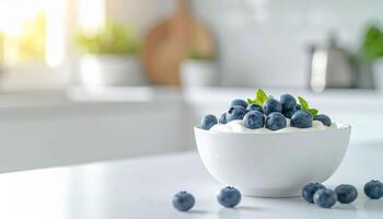 Bowl of creamy yogurt topped with fresh blueberries and mint leaves sits on bright kitchen counter photo