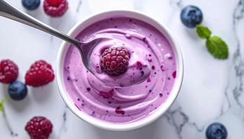Creamy berry yogurt in white bowl with fresh raspberries and blueberries on marble surface photo