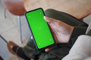 Person holding smartphone with green screen in modern cafe setting photo
