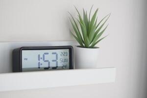 Digital clock and potted plant on a modern wall shelf at home photo