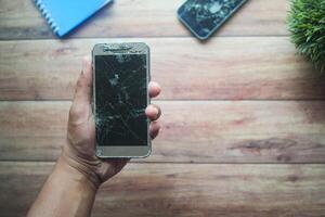 Broken smartphone held in hand on wooden table photo