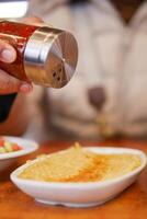 Person adding spice to food at a dining table photo