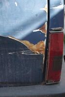 Old car with scratched paint and rust damage in urban area photo