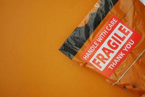 Delivery package with fragile label against an orange wall photo