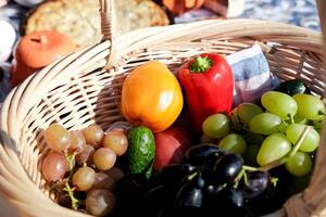 picnic basket with different types of grapes, red pepper, tomatoes and cucumber, close-up outdoors photo