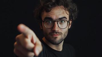 Portrait of a man with glasses pointing his finger directly at the viewer in a dark setting photo