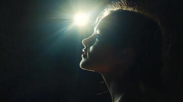 Woman's silhouette with bright light shining above her in a dark background looking upwards intently photo