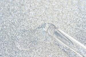 Transparent glass dropper on sparkling silver glitter background texture shine. photo