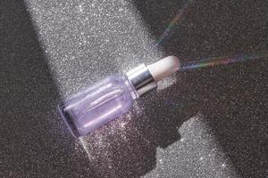 Glittering serum bottle with light prism effect on sparkling surface. photo