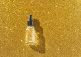 Transparent dropper bottle on sparkling gold background with shimmering glitter texture. photo
