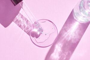 Close-up of glass dropper with skincare serum on pink background in soft light reflection. photo