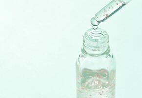 Clear glass dropper bottle with liquid and bubbles against a light green background. photo