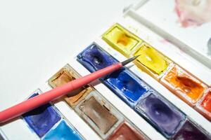 Colorful watercolor palette and brush on white table for artistic painting projects. photo
