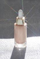 Elegant glass serum bottle with dropper cap sparkling on shimmering surface in sunlight. photo