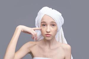 Young caucasian female with under eye patches and towel turban on gray background. photo