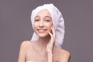 Smiling young caucasian female with towel on head applying skincare in studio setting. photo