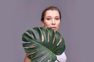 Caucasian adult female posing with monstera leaf against gray background. photo