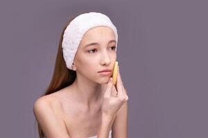 Young caucasian female using facial cleansing tool for skincare routine on gray background. photo