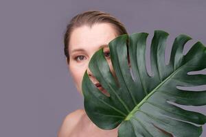 Mature caucasian female partially hidden by large monstera leaf on gray background. photo