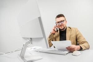 A businessman, call center manager, or entrepreneur consults a client on the phone in a bright office at a computer. The concept is remote work photo