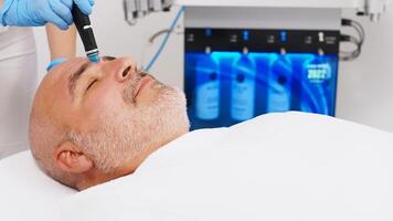 Man undergoes hydro facial vacuum facial cleansing, rejuvenation, moisturizing facial procedure in a beauty clinic. Microdermabrasion procedure in a beauty spa salon. Cosmetology concept photo