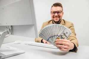 A young businessman in glasses enjoys a large sum of cash in his hands in a modern office. The concept is to convey the feeling of achieving financial independence and success in business photo