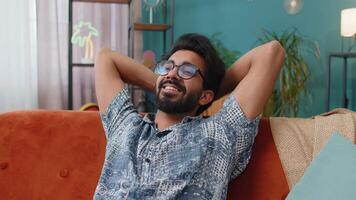 Tired indian man lying down on comfortable couch, taking a rest, daytime nap relaxing falling asleep video