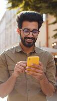 Indian man use smartphone typing text messages browsing internet finishing work chatting online video