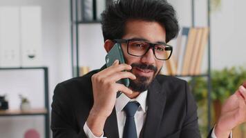 Indian business man working, having mobile phone talk at office workplace using messenger chat apps video