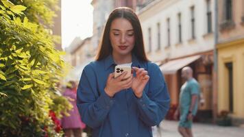 Young woman use smartphone typing text messages browsing internet finishing work looking at camera video